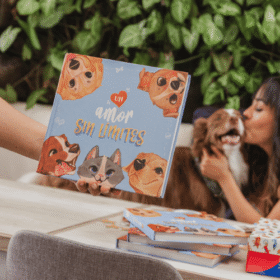 A person holds up a blue children's book with cartoon dogs around the title 'amor sin límites'; a woman hugs a dog in the background.